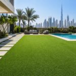 Artificial grass installation in Dubai showing a modern villa lawn with green turf, poolside seating, and city skyline background